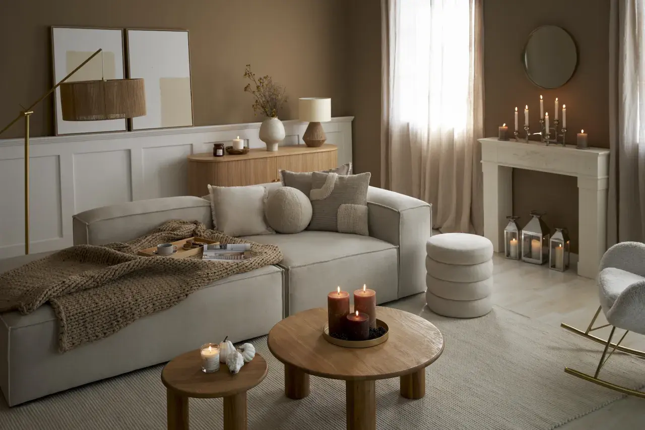 Przytulny salon w odcieniach sepia kolor. Miękki narożnik, drewniane stoliki, kominek z ozdobnymi świecami i ciepły pled tworzą atmosferę relaksu.