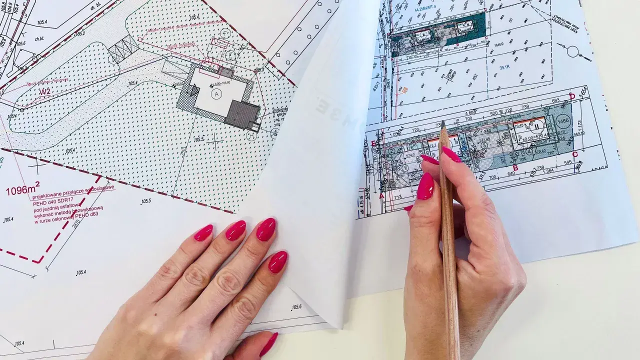Ręce z różowym lakierem przeglądają mapę do celów projektowych, zaznaczając ołówkiem szczegóły.
