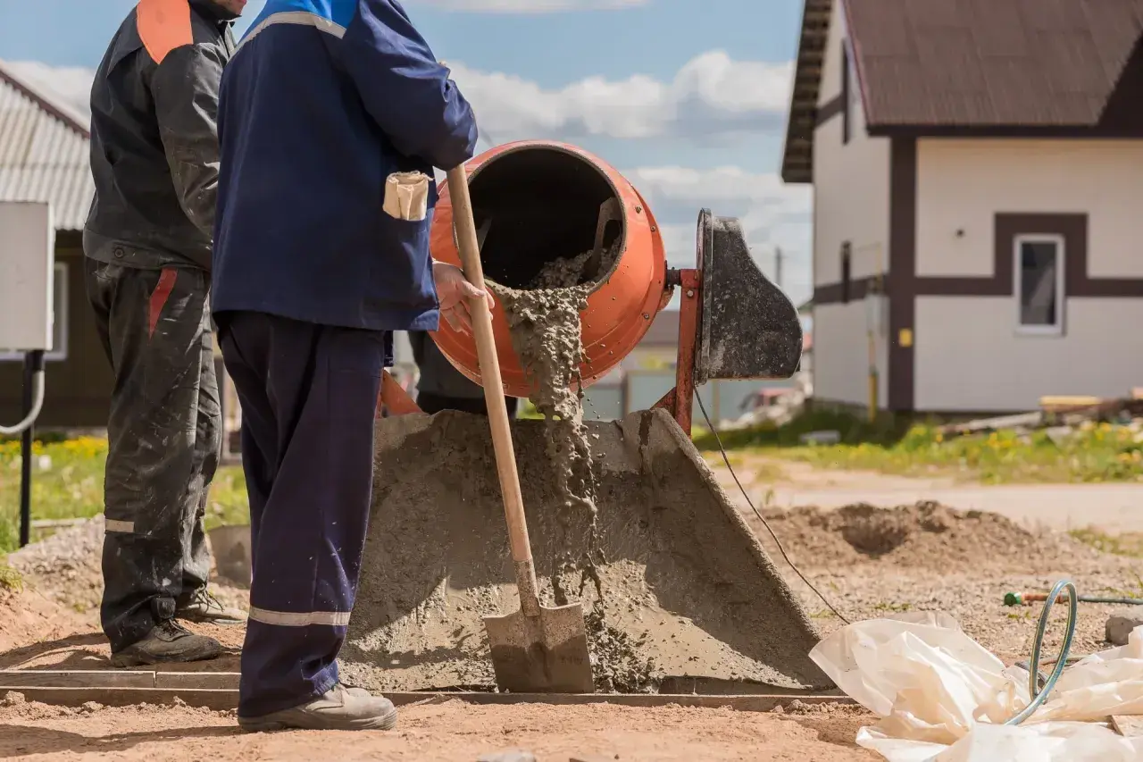 Robotnicy mieszają beton. Zastanawiasz się, ile kosztuje worek cementu na budowie?