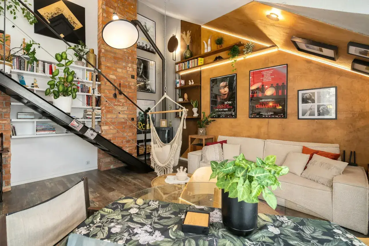 Salon w stylu loftowym z ceglaną ścianą, metalowymi schodami, wiszącym fotelem i przytulną kanapą.