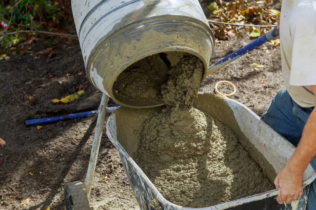 Mieszarka wylewa świeży beton do taczki. Właściwe proporcje betonu są kluczowe dla trwałości budowli.