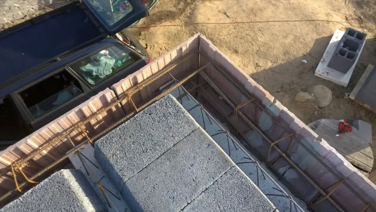 Szalowanie stropu z bloczków betonowych i zbrojenia. Obok stoi samochód.