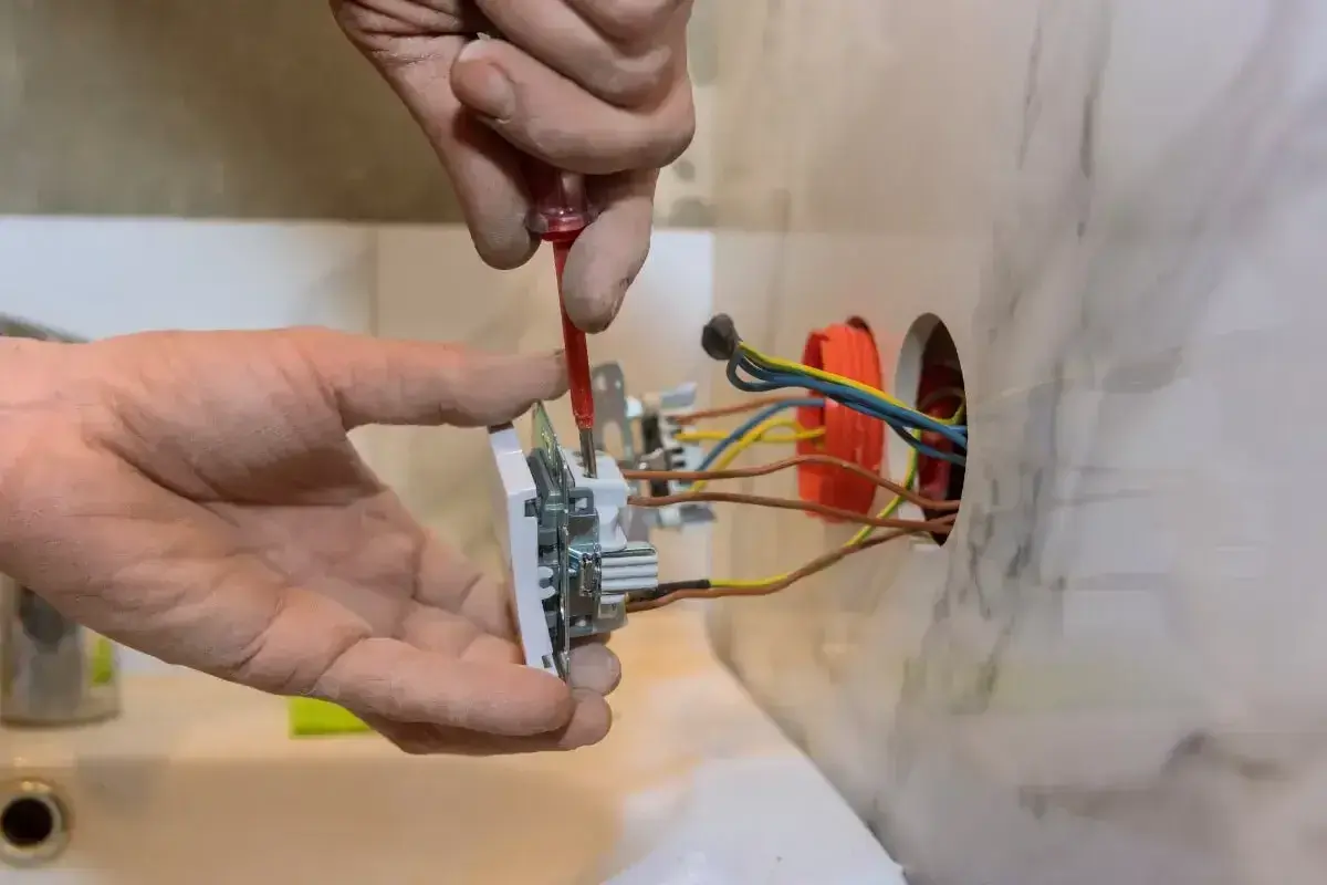 Instalator przykręca gniazdko, pokazując, jak podłączyć gniazdko. Widać przewody elektryczne i narzędzia.