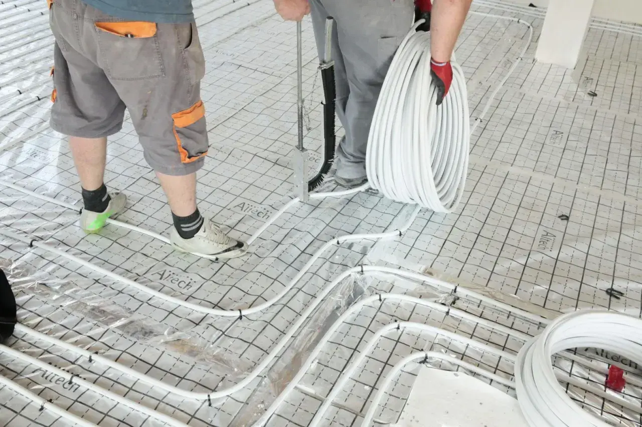 Pracownicy układają rury do ogrzewania podłogowego na siatce, przygotowując podkład pod jastrych.