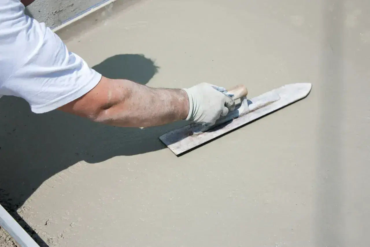 Ręka w rękawiczce wygładza świeży beton na tarasie.