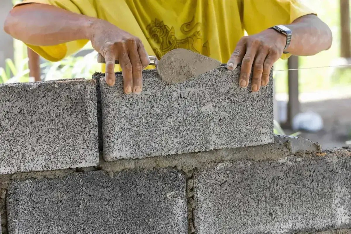 Murarz układa bloczek betonowy, sprawdzając jego wymiary.