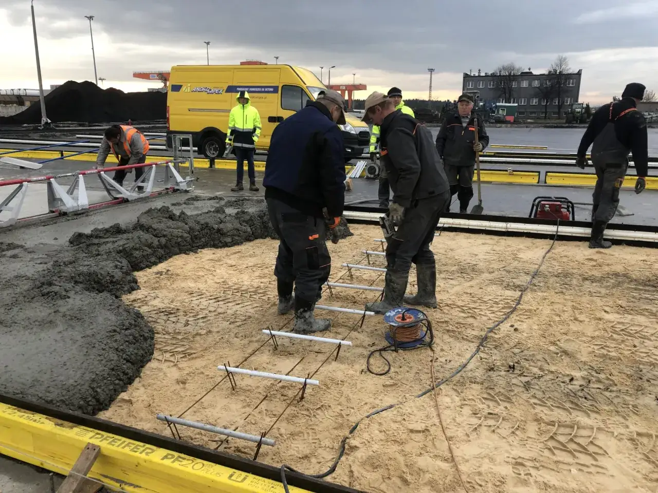 Budowlańcy pracują przy wylewaniu betonu. Widać zbrojenie i żółtą trelinkę.