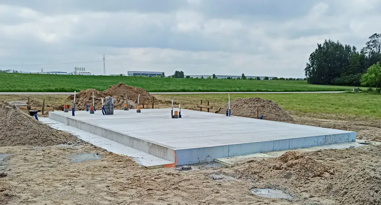 Solidny fundament budowy, z wystającymi rurami i otoczoną piaskiem, zapowiada przyszły dom.
