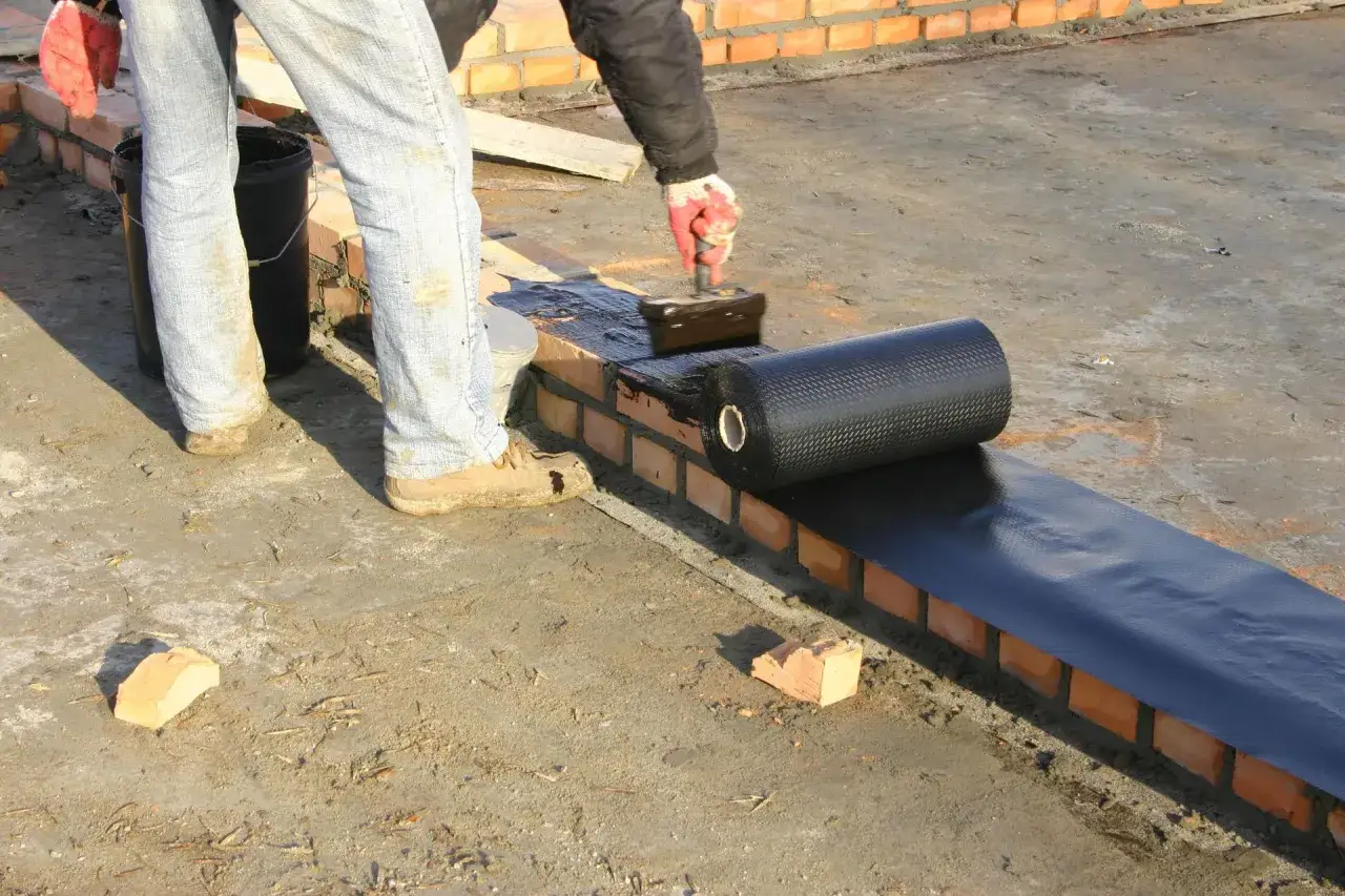 Pracownik nakłada abizol na ceglaną ścianę, przygotowując ją do dalszych prac.