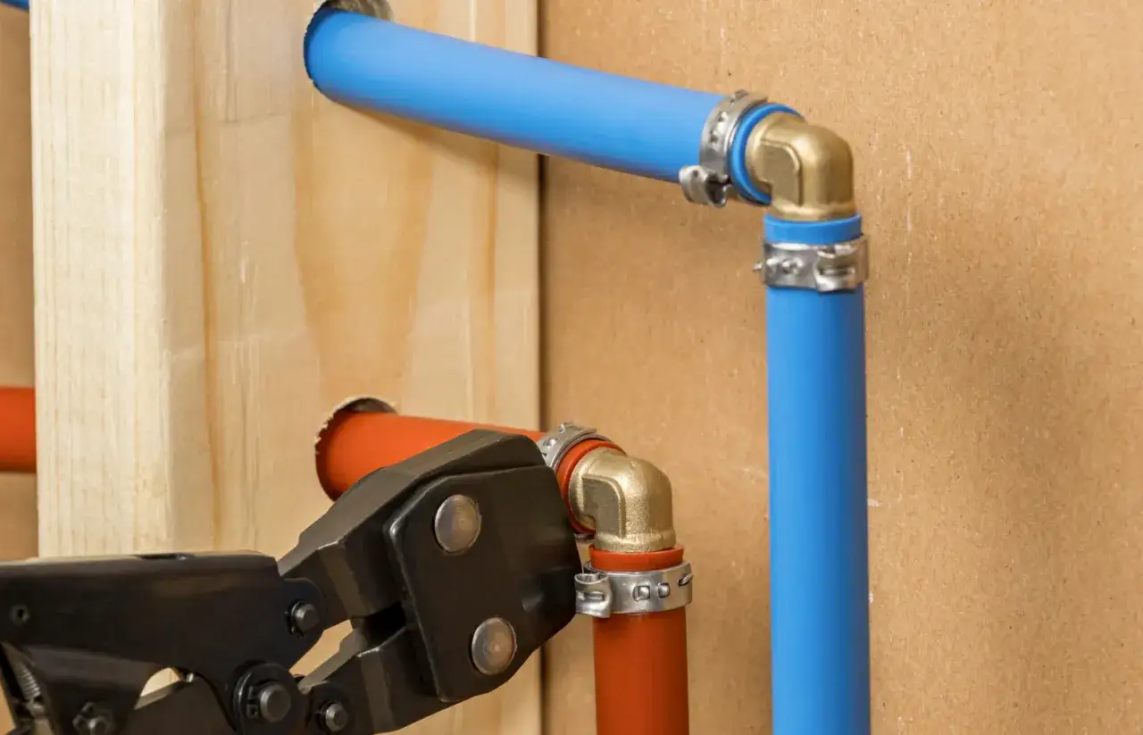 Instalacja hydrauliczna z rurami pex. Narzędzie do zaciskania łączy pomarańczową rurę z mosiężnym kolankiem.