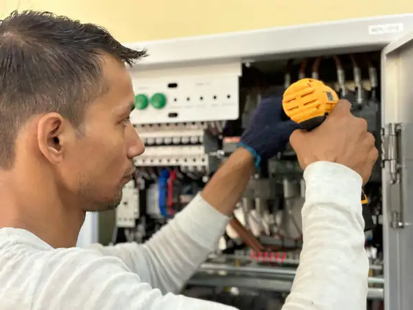 Elektryk pracuje przy panelu sterowania, unikając przeciążenia systemu.