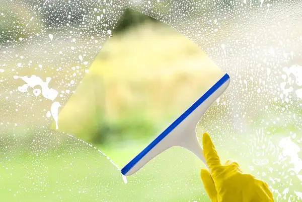 Ręka w żółtej rękawiczce czyści okno squeegee. Sprawdź mycie okien cennik, by mieć lśniące szyby.
