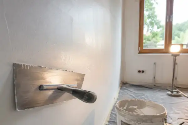 Gładka ściana po nałożeniu masy gipsowej. Narzędzie do tynkowania i wiadro z masą czekają na dalsze prace.