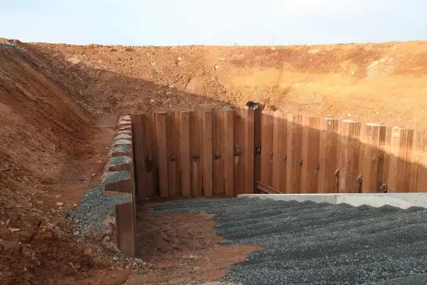 Konstrukcja oporowa typu larsen stabilizuje wykop. Widoczne są stalowe ścianki szczelne i nasypy.